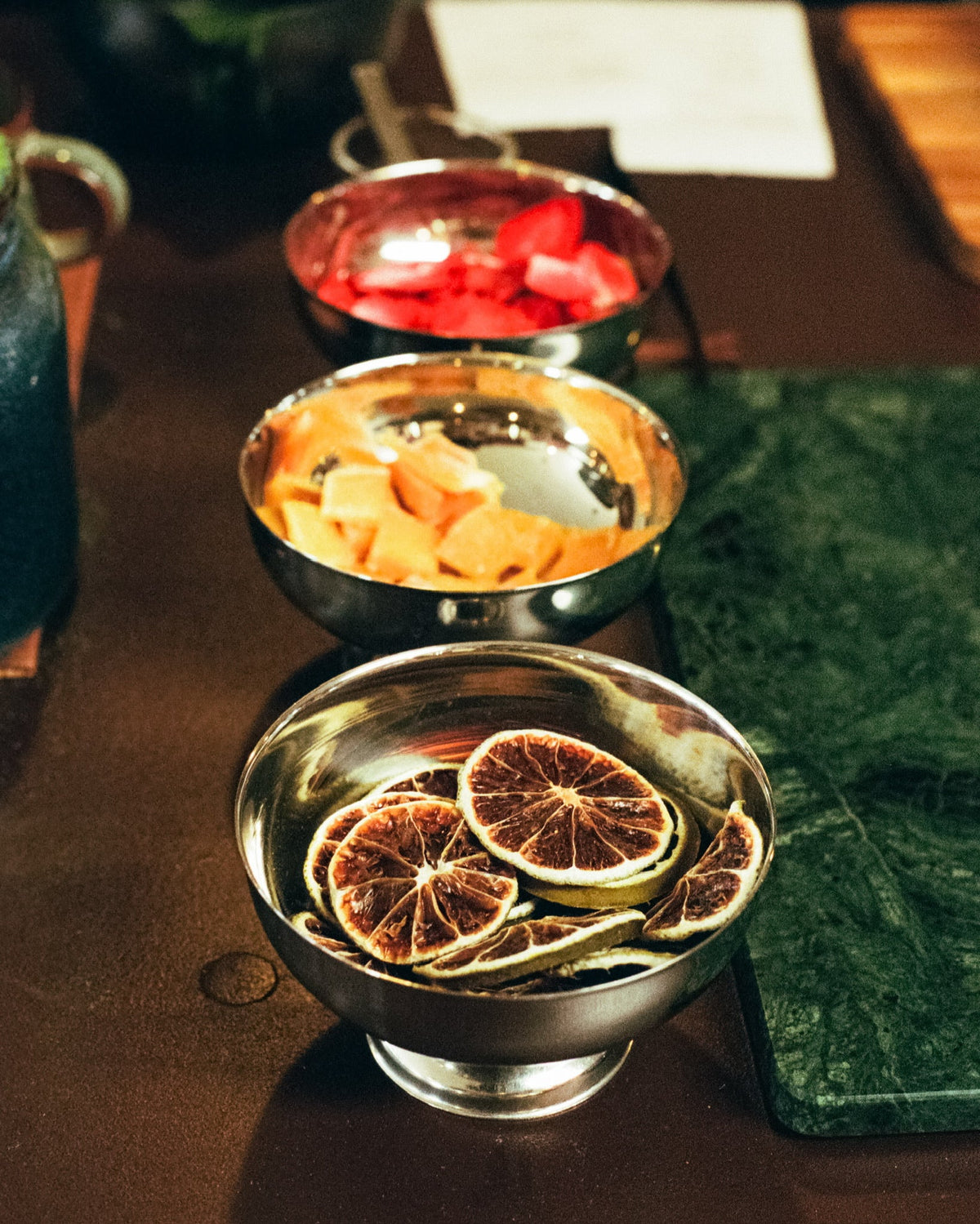Metal bowls of fruit garnishes, including dried orange slices, arranged on the Infusion Lab counter.